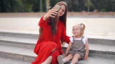 Mutlu anne, güzel kızıyla bahar parkında selfie çekerken elinde akıllı telefon tutuyor. Güzel bir aile birlikte güzel bir anın tadını çıkarır. Anne ve çocuk arasındaki sevgi dolu ilişki.