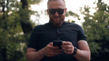 Şaşırmış mutlu iş adamı iyi haberlerle SMS mesajı alıyor. Parkta yürürken akıllı telefona bakarak başarıyı kutlayan heyecanlı mutlu adam. Zafer için mobil konsept