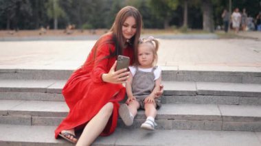 Bir aile parkta yürürken selfie çeker. Güzel, genç bir anne elinde akıllı bir telefonla kızına sarılıyor. Kaygısız anne hafta sonunun tadını çıkarıyor, tatilleri tatlı bebekle geçiriyor. Çocukluk anıları
