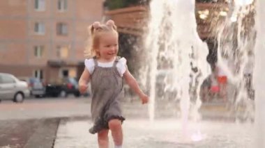 Bir baba gün batımında fıskiyeden suyla parkta ona koşan küçük kızına sarılır. Aile mutluluğu. Çocuk çok mutlu ve neşeli. Güzel bir hayat konsepti. Yavaş çekim.