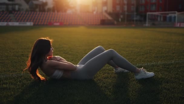 美しい細い若い女性がスタジアムで屋外でスポーツをしています スポーツウェアの女の子が彼女の腹筋を振る スローモーション — ストック動画