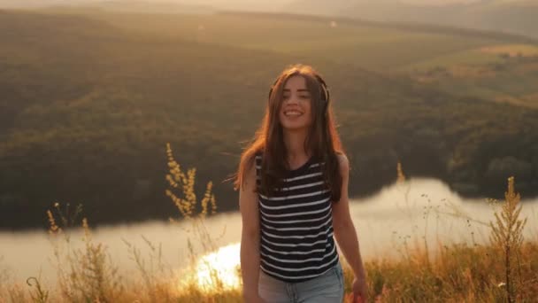 Usmívající Dlouhosrstá Dívka Sluchátkách Kráčející Vrcholku Kopce Při Západu Slunce — Stock video