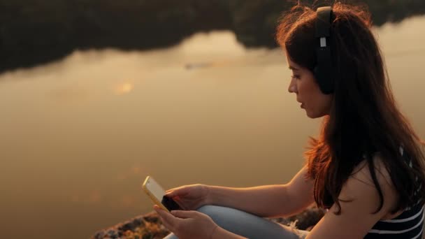 Young Attractive Smiling Woman Sits Top Rock River Listens Music — Stock Video