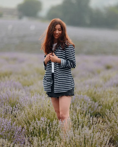 Akşama lavanta tarlasında kısa elbiseli ve gömlekli güzel bir kadın. Yazın gün batımında. Kırsal doğa çiçekleri.
