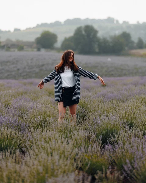 Genç, çekici, rahat bir kadın lavanta tarlasında durup güneşli bir günde kollarını açmış güzel doğa ve manzaranın tadını çıkarıyor.