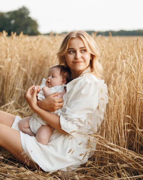 Çekici, genç bir kadının portresi hasır şapkalı ve beyaz elbiseli sarışın, olgun altın buğday tarlasında küçük kızını gün batımında kollarında tutuyor.