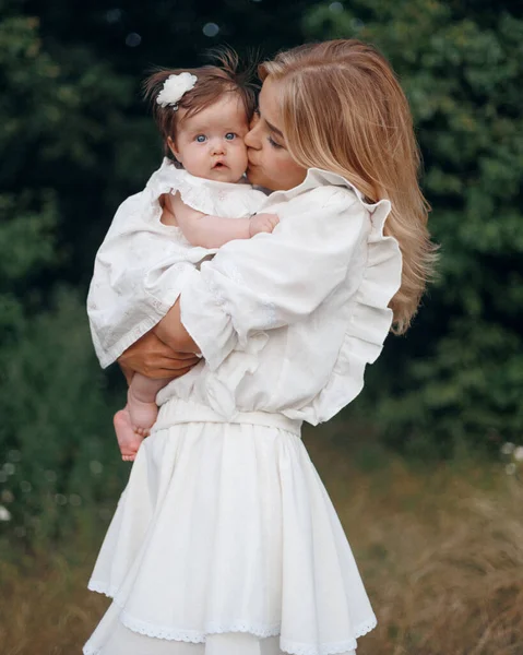 Güzel, genç bir anne yazın bebeğiyle dışarıda oynuyor, anne ve küçük kızı yürüyor, açık hava eğlencesi, anneden bebeğe sevgi ve öpücük.
