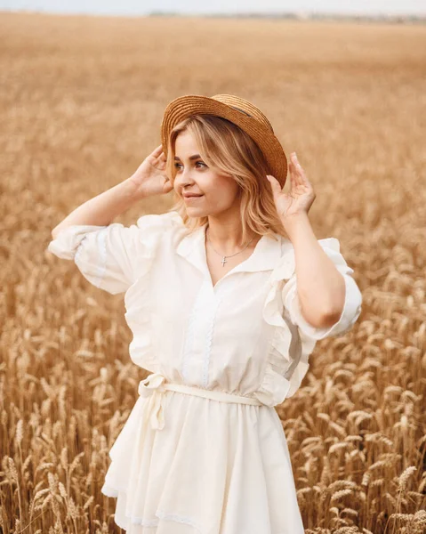 Çekici bir kızın portresi hasır şapkalı sarışın ve gün batımında olgunlaşmış altın buğday tarlasında beyaz bir elbise giyen