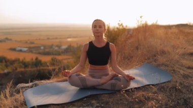Lotus pozisyonunda oturan genç bir kadın. Gözleri kapalı. Gün batımında yoga yapıyor.