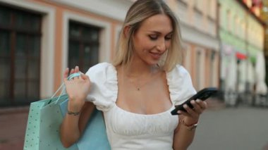 Genç, güzel, sarışın bir kadın. Yazlık elbisesiyle alışveriş torbalarıyla şehir caddesinde duruyor. Akıllı telefona bakıyor ve okunan mesajdan mutlu bir şekilde gülüyor.