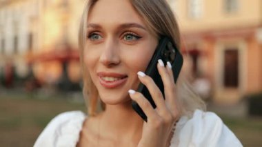 Çekici, genç, sarışın, gülümseyen, uzun saçlı, dışarıda cep telefonuyla konuşan kadının yüzünü kapatın.