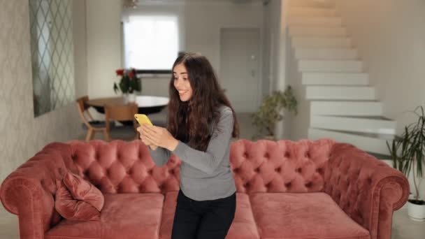 Akıllı Telefonundaki Haberle Heyecanlanan Genç Kadın Kanepede Oturarak Şansının Dönümünü — Stok video