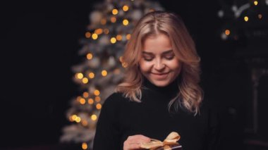 Noel ağacının arka planında, Noel arifesinde el ele tutuşmuş ışıklarla gülümseyen, neşeli, çekici, çekici, sarışın bir kadının portresi.