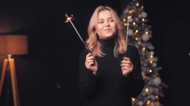 Elinde maytap tutan genç bir kadının portresi ve arka planda Noel ağacının ışıklarında, Noel arifesinde, yeni yıl arifesinde dans ederek eğleniyor.