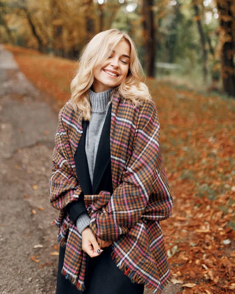 Atkısı olan neşeli genç bir kadın arka planda sarı ağaçlarla parkta dinleniyor. Gülümseyen güzel kız sonbahar mevsiminde güneşli havanın tadını çıkarıyor. Mutlu, güzel, doğal kadın gülüyor