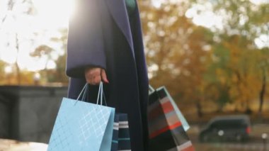 Gün boyunca şık bir ceket ve kot pantolon giymiş, uzun bir alışveriş gününden sonra renkli alışveriş torbaları tutan kadın bacaklarını kapatın. Sonbahar parkında alışveriş meraklısı modası.