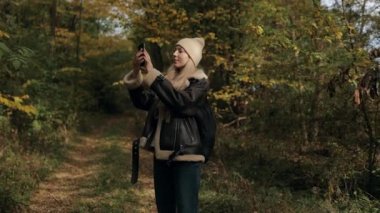Güz Ormanı 'nda Genç Kadın Turist Akıllı Telefonla Fotoğraf Çekiyor. Sonbahar Ormanında Yürüyen Kadınlar Doğanın tadını çıkarıyor.