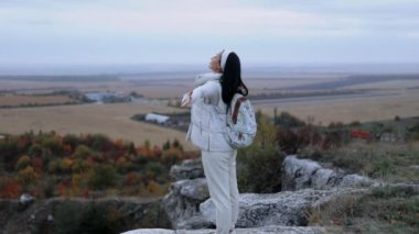 Uzun saçlı genç bir kadın, elleri havada bir kayanın üzerinde duran bir turist. Sonbahar doğasının güzel manzarası