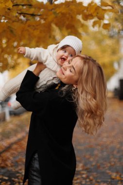 Sonbahar yürüyüşüne çıkmış mutlu bir aile! Anne ve küçük kız bebek parkta yürüyor ve güzel sonbahar doğasının tadını çıkarıyorlar..