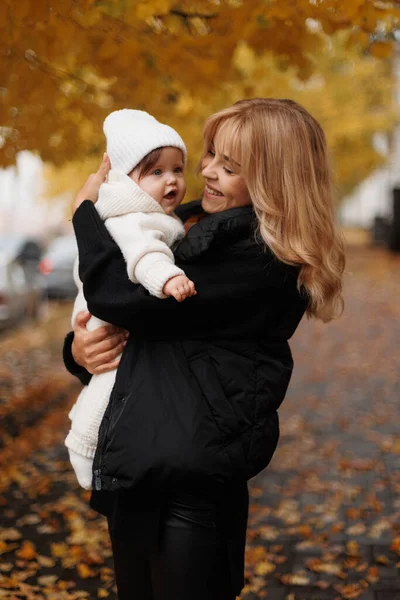 Küçük kızıyla birlikte mutlu, genç, güzel bir anne sonbahar zamanı renkli yapraklarla şehir parkında eğleniyor. Mutlu aile, anneler günü konsepti.