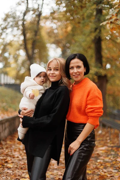 Büyükannesi ve kızı sonbahar parkında yürürken birbirlerine sarılıyorlar.