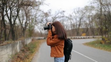 Güzel bir kadın fotoğrafçı ormanda yol boyunca fotoğraf çekiyor. Turist kadın kuşları, hayvanları, manzarayı vuruyor. Sırt çantalı bir turist kız ormanda fotoğraf çekiyor.