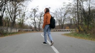 Güzel turist genç bayan çantasıyla kır yolunda yürüyor ve doğaya bakıyor. Yüksek kalite 4k video