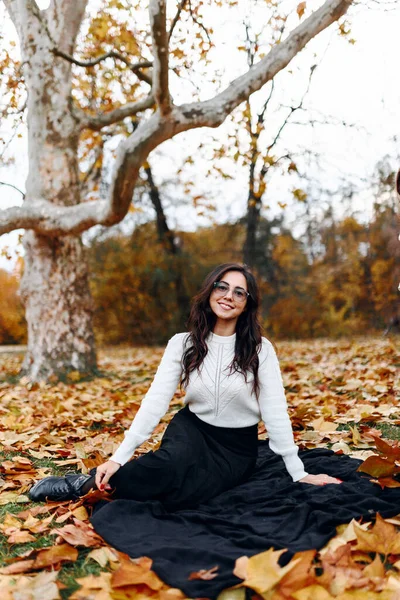 Güz parkının çimlerinde oturmuş, güzel bir kadın portresi olan kameraya bakıyor.