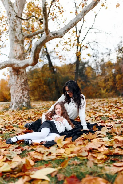 Mutlu aile: anne ve çocuk küçük kız güz yürüyüşü sırasında çimenlerde oturup göl kenarında eğleniyor, gülümsüyor, yürüyüş yapıyor, anne ve kız birbirlerini seviyorlar.