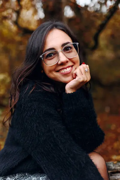Güz parkının arka planında gözlük takan güzel bir kız kameraya bakıyor, güzel bir kadın portresi, hoş bir gülümseme, yakın çekim.