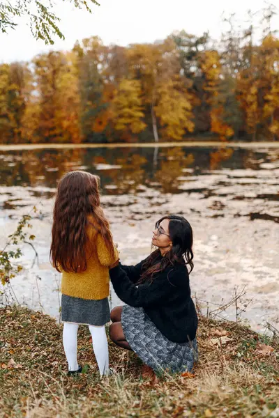 Mutlu aile: anne ve çocuk küçük kız sonbahar doğasında kucaklaşır göl kenarında yürür, eğlenir ve güler, birlikte yürür, anne ve kız sever