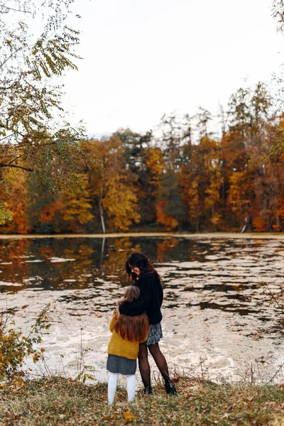Mutlu aile: anne ve çocuk küçük kız sonbahar doğasında kucaklaşma göl kenarında yürüyüş, eğlenme ve gülümseme, birlikte yürüme, anne ve kız