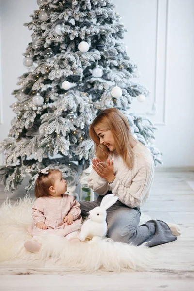 Anne ve küçük kızı Noel ağacının yanında oturuyorlar. Aile yeni yılı kutluyor. Anne ve kızı oynuyorlar ve eğleniyorlar.