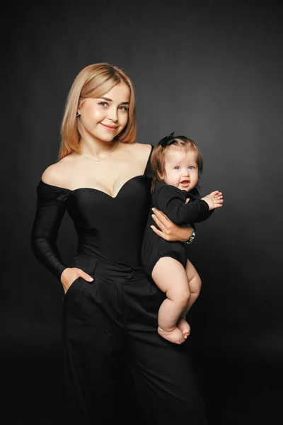 Siyah arka planda, gülümseyen bir annenin kucağında ve kucağında küçük tatlı bir kız çocuğunun yakın plan portresi. Mutlu ebeveynler anneliğin tadını çıkarırlar. Bir anne ve küçük bir çocuk arasındaki ilişki..