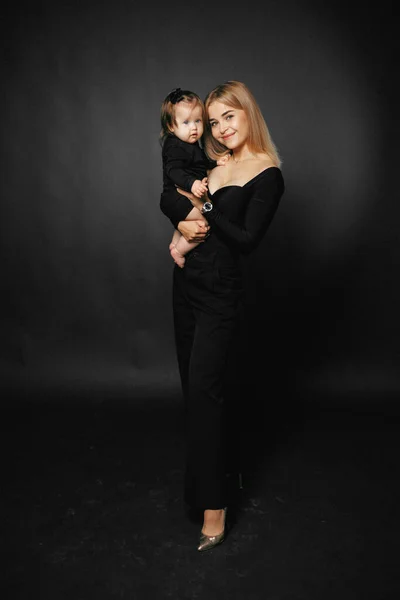 Siyah arka planda kucağında tatlı bir kız çocuğu taşıyan gülümseyen bir annenin portresi. Mutlu ebeveynler anneliğin tadını çıkarırlar. Bir anne ve küçük bir çocuk arasındaki ilişki. Aile ve çocuk bakımı kavramı