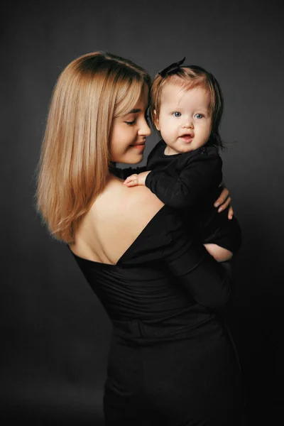 Siyah arka planda, gülümseyen bir annenin kucağında tatlı bir kız çocuğu resmi. Mutlu ebeveynler anneliğin tadını çıkarırlar. Bir anne ve küçük bir çocuk arasındaki ilişki. Aile ve çocuk bakımı dolandırıcılığı