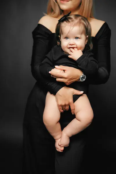 Siyah arka planda kucağında tatlı bir bebek taşıyan genç bir annenin portresi. Mutlu ebeveynler anneliğin tadını çıkarırlar. Bir anne ve küçük bir çocuk arasındaki ilişki. Aile ve çocuk bakımı kavramı