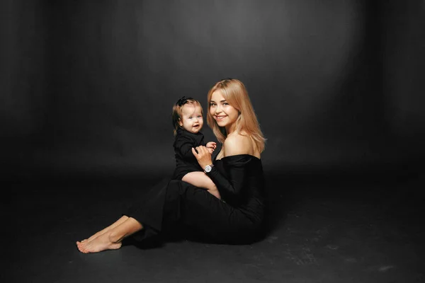 Küçük kızını kollarında tutan genç bir annenin portresi. Stüdyoda siyah bir arka planda otururken sarılıp gülümsüyor.