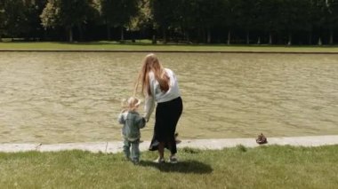 Bir anne ve küçük kızı Versailles Park 'ta göl kenarında yürüyüp vahşi ördeklere bakıyorlar. Anne ve çocuk dışarıda yürüyorlar, dikiz aynasından.