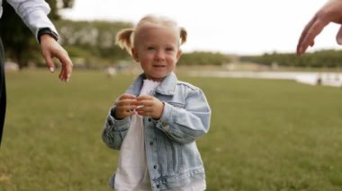 Parkta yürüyen gülümseyen bir adam ve kadının, küçük kızlarının ellerini tutarken ön görüntüsü. Birlikte zaman geçirmek, aile hafta sonu, parkta piknik. Yavaş çekim