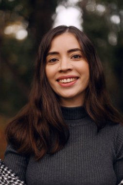 Güz parkında, sevimli, gülümseyen, genç bir bayanın yakın portresi, kamerana bakıyor, kahverengi saçlı.