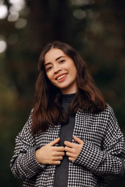 Güz parkında, kahverengi saçlı, elbiseli ve montlu, gülümseyen güzel bir genç kızın yakın plan portresi.