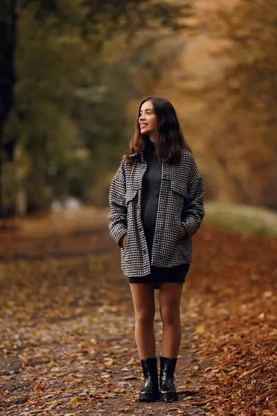 Güzel, gülümseyen genç bir kızın portresi. Uzun boylu, kahverengi saçlı, elbiseli ve montlu, sonbahar parkında.