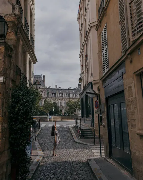 İnce, yaz elbisesi içinde genç bir kadın turist eski Paris sokaklarında yürüyor, şehrin antik mimarisinin tadını çıkarıyor.