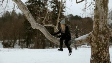 Karlı bir ormanın arka planında bir kadın bir ağaç dalında oturuyor. Noel ve yeni yıl tatili, şenlikli bir gün, karlı soğuk bir gün, kız mutlu ve keyfi yerinde.