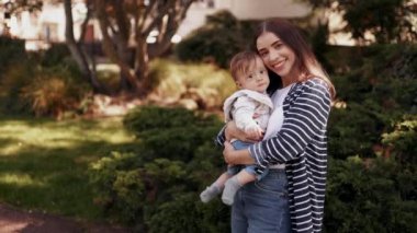 Mutlu anne ve oğulun yakın plan portresi, çocuk kucaklaşması, birbirine dokunması, gülüşmeler, kameraya dişlek bir gülümsemeyle bakmak, aile ilişkisinden keyif almak, annelik, çocukluk, açık havada yakınlık. yavaş çekim