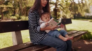 Genç, beyaz, güzel bir kadın ebeveyn. Küçük, şirin bir odada yeni doğmuş bebeğe kitap okuyor. Evde annesiyle oturup kitaba bakan sevimli bir bebek. Güzel anneyle bebek bağı. Aile kavramı. Kapat.
