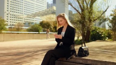 Genç bir iş kadını elinde akıllı bir telefonla bankta oturuyor, kısaca merhaba demek için yukarı bakıyor dostane bir gülümsemeyle, sonra bakışlarını ekrandaki gündelik ve sıcak kentsel ana çeviriyor..