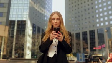 Akıllı telefon kullanan takım elbiseli bir kadın. Büyük bir şehirde müdür. İnternette insanlarla iletişim kurmak, mesajlaşmak ve internette gezinmek. İş bölgesindeki binaların arka planlarına karşı. 