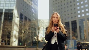 Şehir caddesinde akıllı telefon kullanan takım elbiseli güzel bir kadının portresi. Büyük bir şehirde müdür. İnternette insanlarla iletişim kurmak, mesajlaşmak ve internette gezinmek. Paris 'in iş bölgesindeki binaların arka planlarına karşı